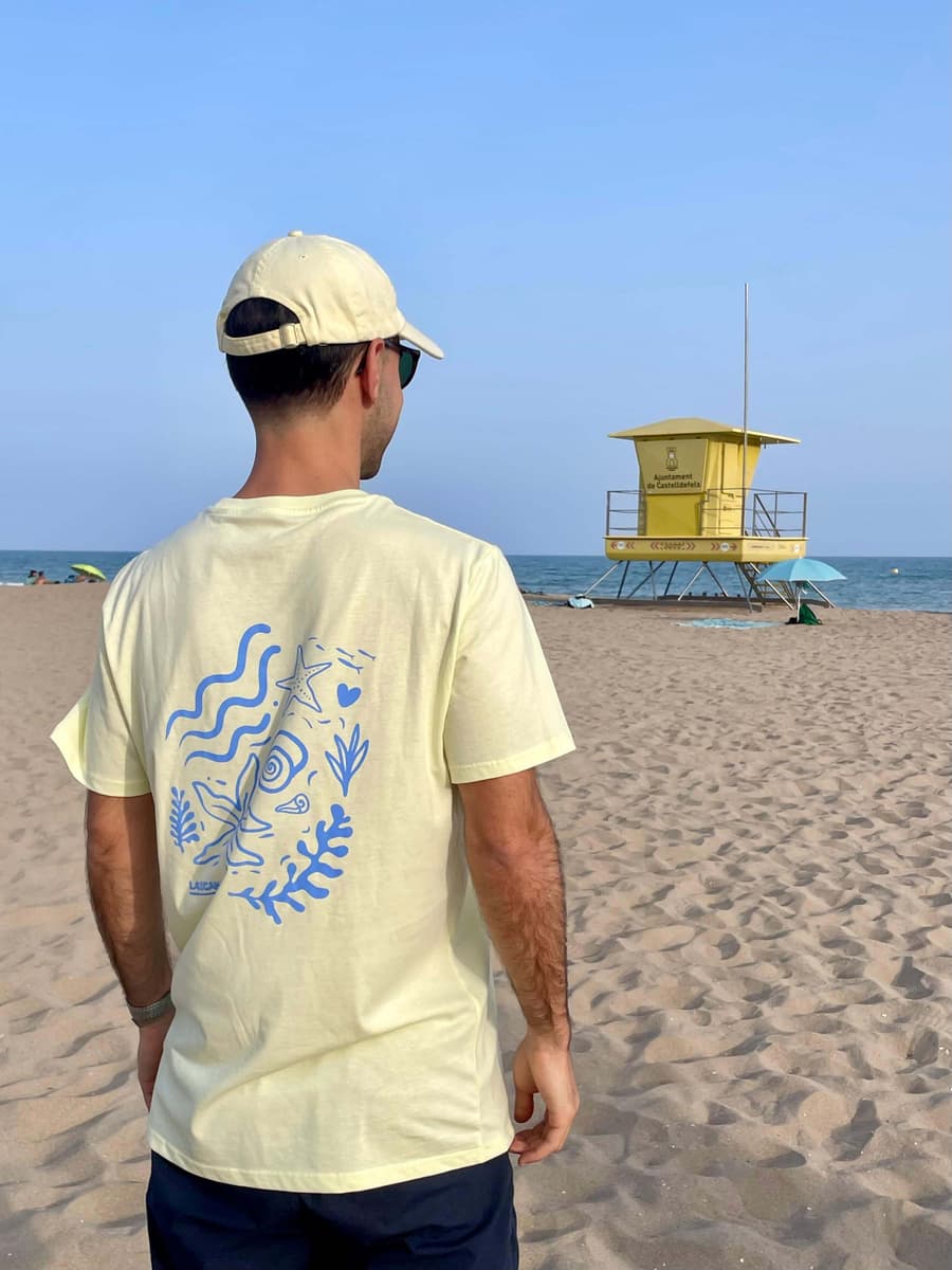 Chico de espaldas con una camiseta serigrafiada de La Cucaña en la playa